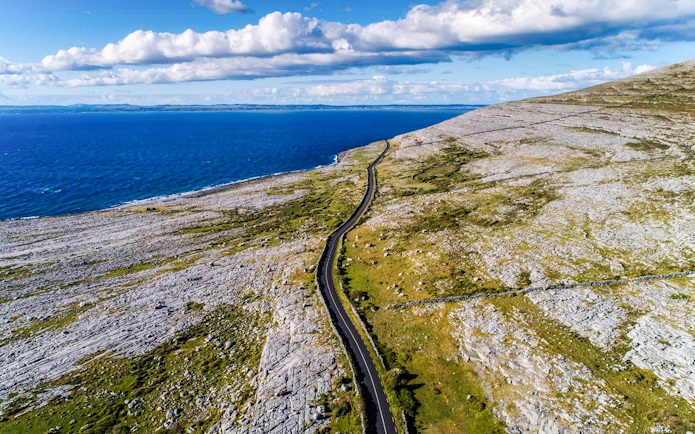 Aerial view of The Burren's coastal landscape with a winding road and ocean.