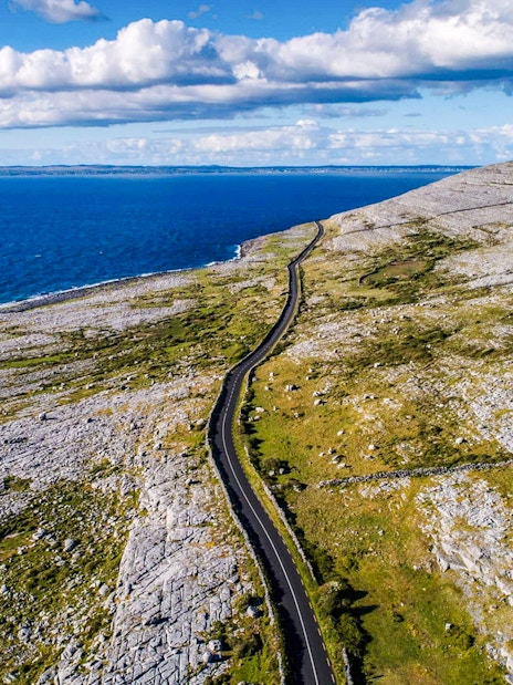 Aerial view of The Burren's coastal landscape with a winding road and ocean.