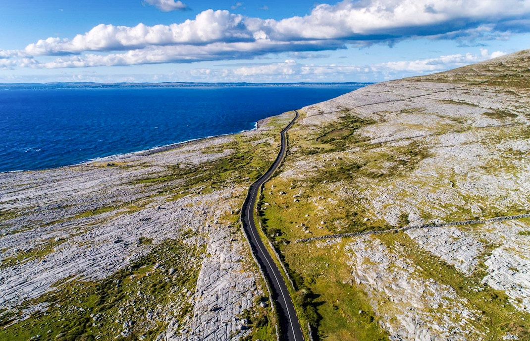 Aerial view of The Burren's coastal landscape with a winding road and ocean.