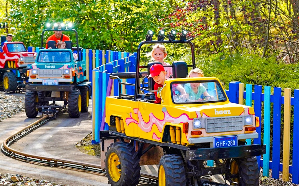 Children enjoying a colorful 4x4 adventure ride on a track through a scenic park.