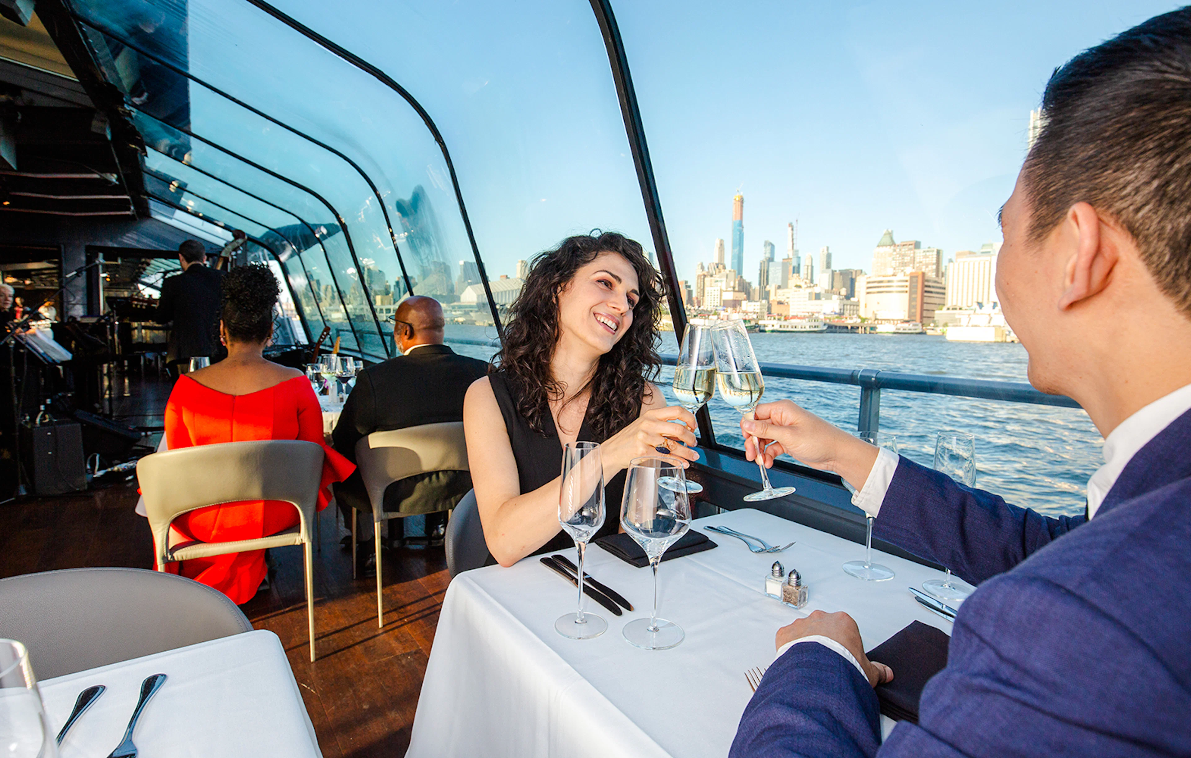 Couple toasting with champagne on New Jersey Signature Cruise with city skyline view.