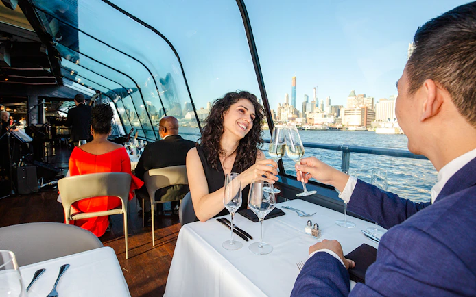 Couple toasting with champagne on New Jersey Signature Cruise with city skyline view.