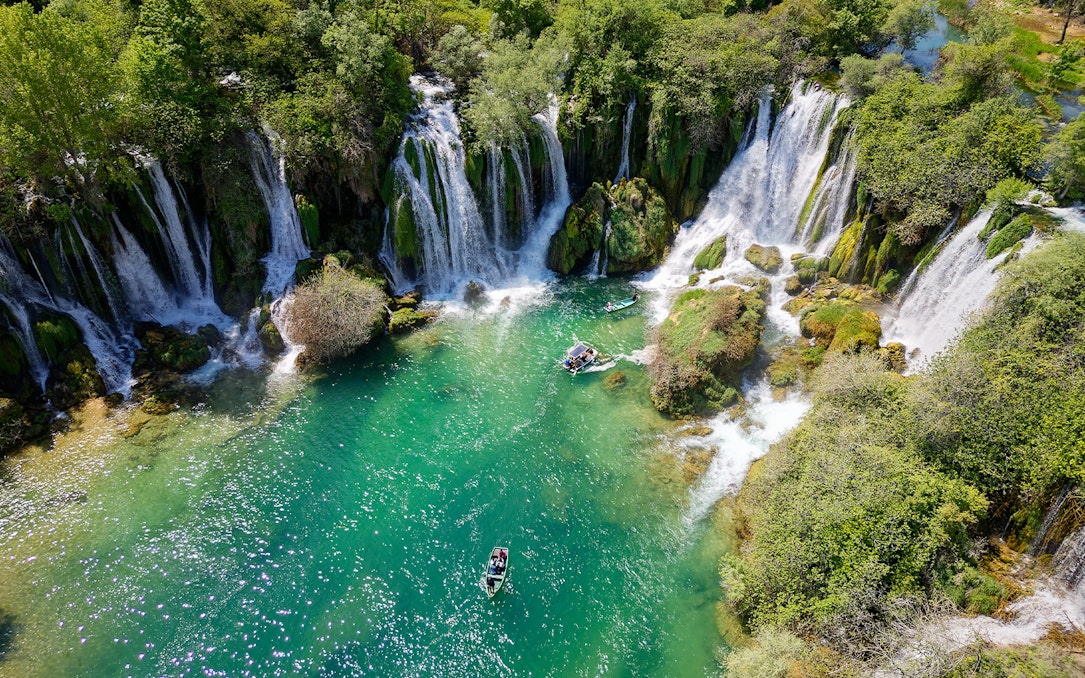 Aerial view of Kravica Waterfall with boats on turquoise water, Bosnia and Herzegovina.