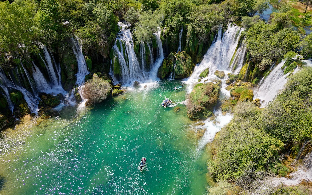 Aerial view of Kravica Waterfall with boats on turquoise water, Bosnia and Herzegovina.
