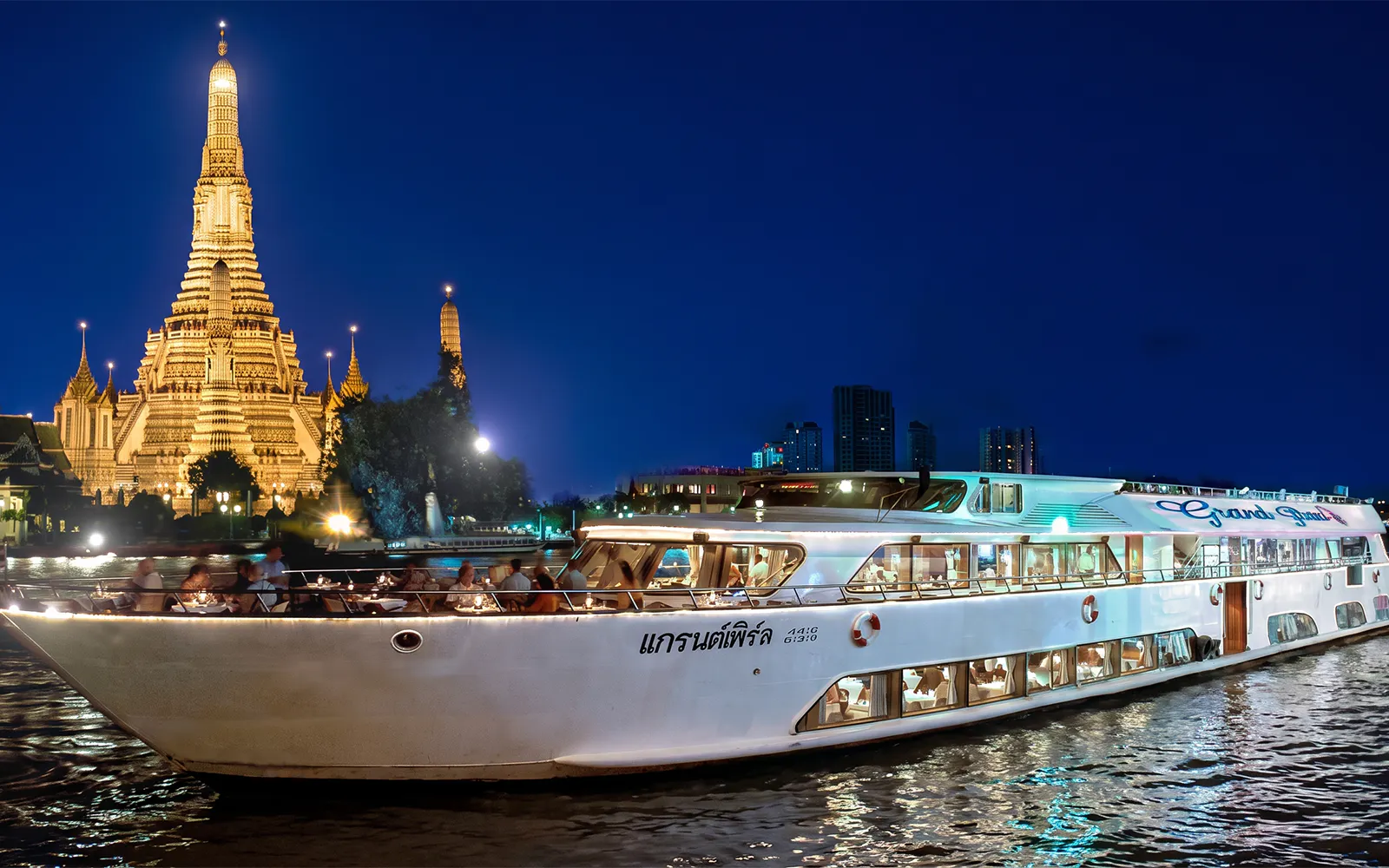 Grand Pearl Cruise sailing past Wat Arun temple in Bangkok at night.