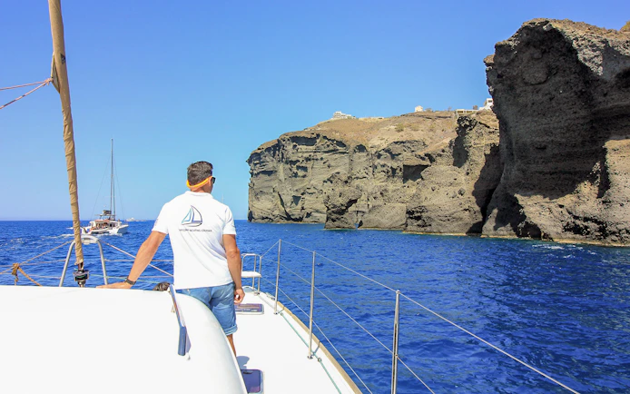 Catamaran sailing near Santorini cliffs on a luxury cruise.