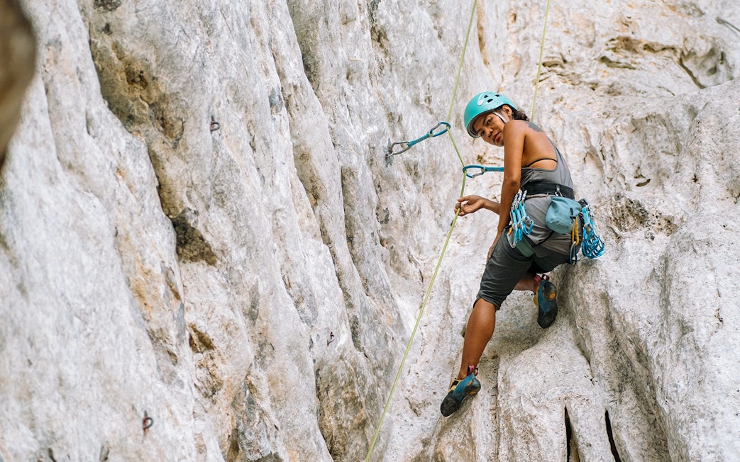 Female climber scaling limestone cliff in Krabi, Thailand.
