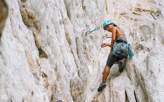 Female climber scaling limestone cliff in Krabi, Thailand.