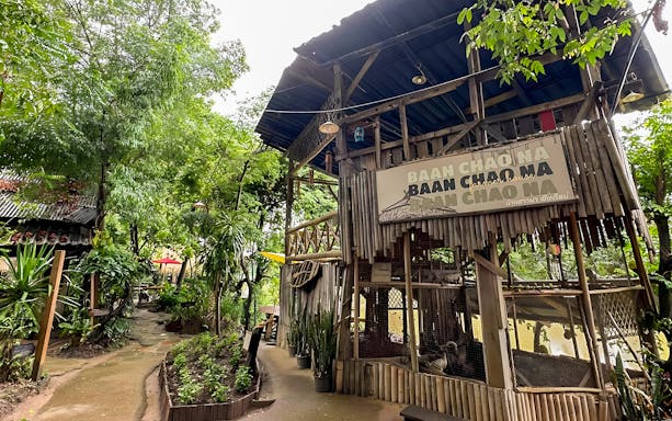 Mae Ping River Cruise stop at Baan Chao Na, featuring lush greenery and rustic wooden structures.