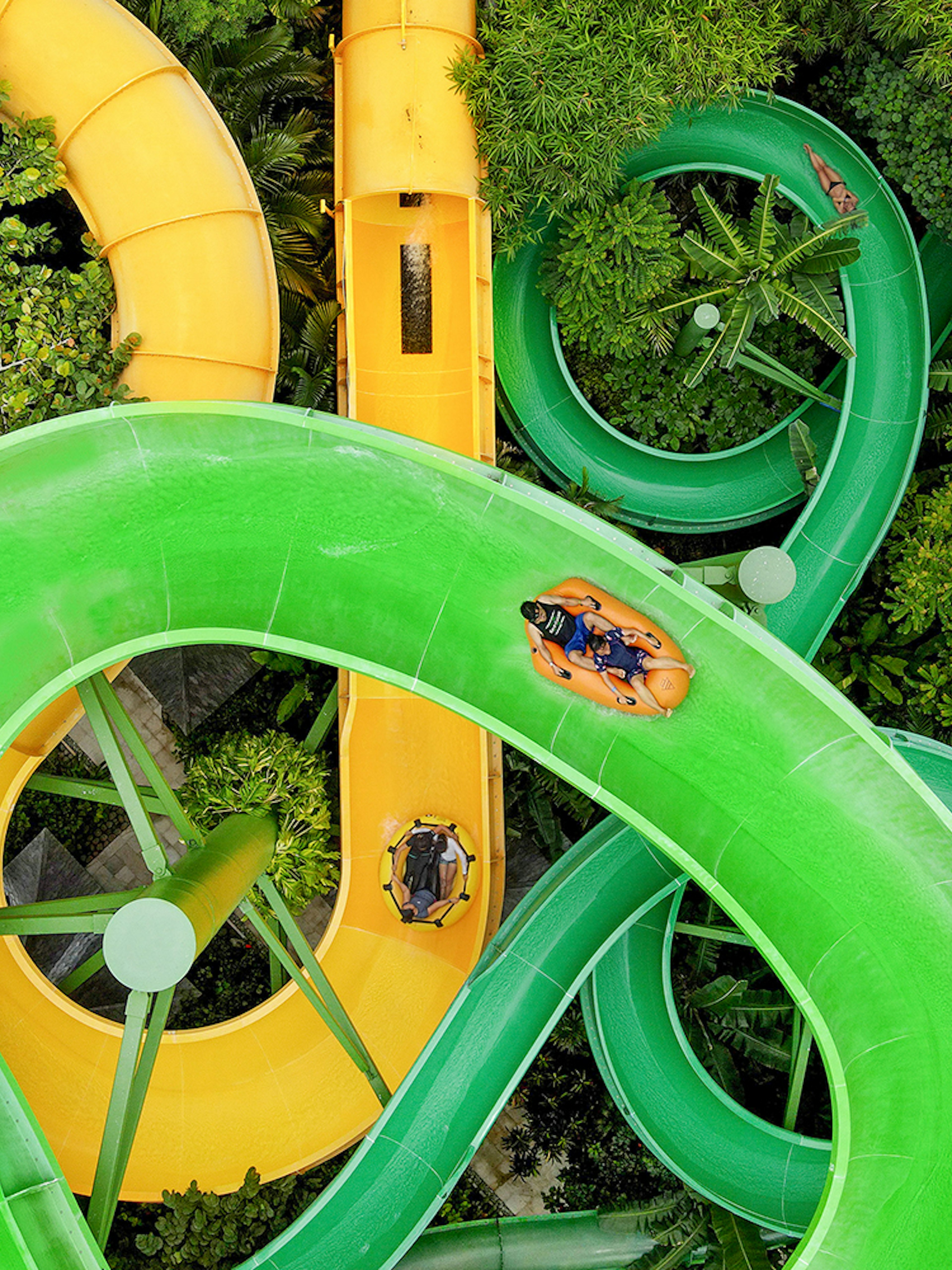 Waterslides at Waterbom Bali with people on inflatable rafts navigating green and yellow slides.