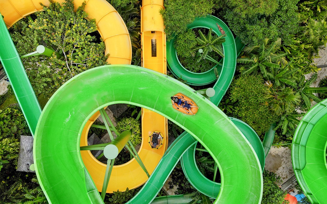 Waterslides at Waterbom Bali with people on inflatable rafts navigating green and yellow slides.