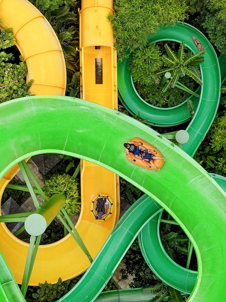 Waterslides at Waterbom Bali with people on inflatable rafts navigating green and yellow slides.
