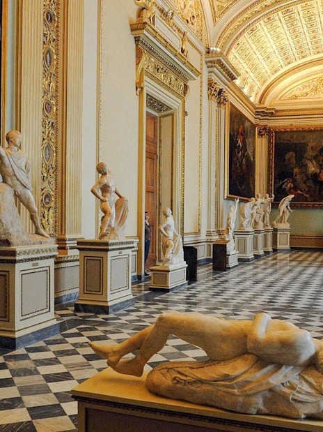 Uffizi Gallery hall with classical sculptures and ornate ceiling.