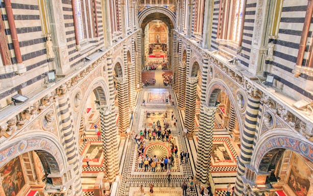 Siena Duomo interior with striped columns and visitors exploring the ornate architecture.