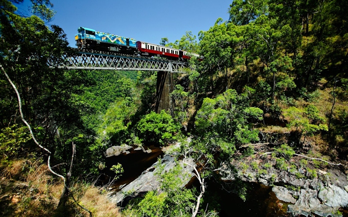 Train crossing a bridge through lush forest on a scenic tour with transfers.