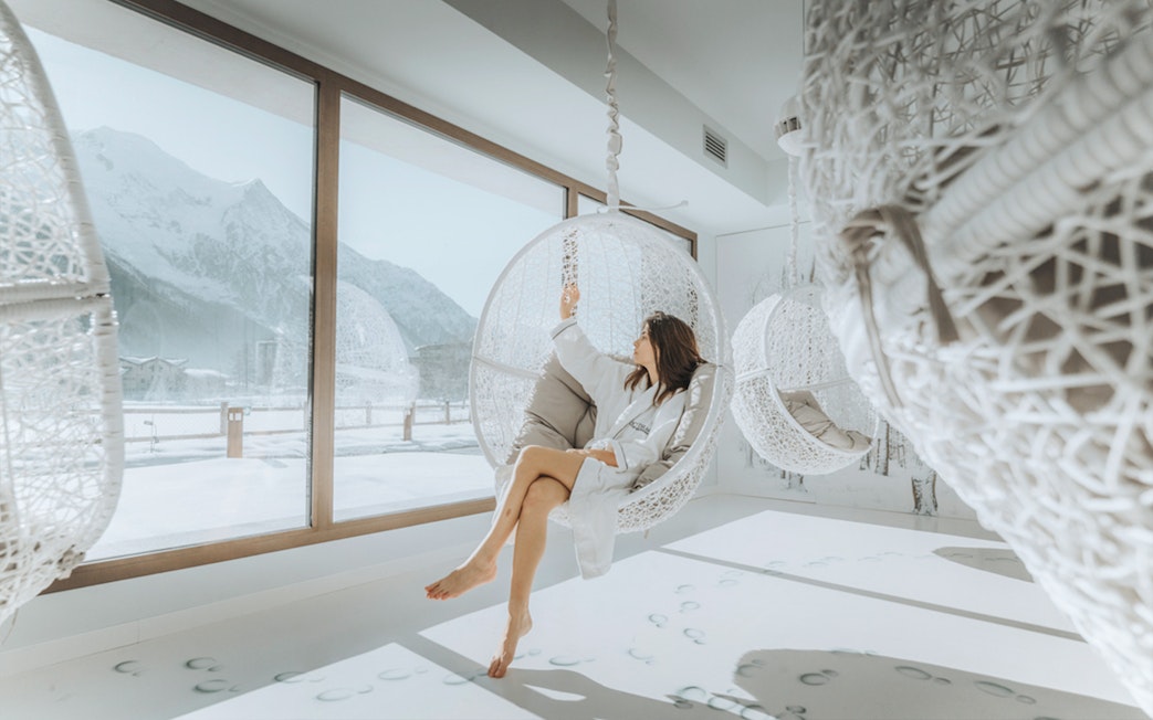 Visitor relaxing in a hanging chair at QC Terme Chamonix Resort & Spa with snowy mountain view.