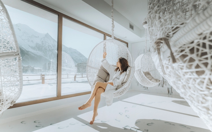 Visitor relaxing in a hanging chair at QC Terme Chamonix Resort & Spa with snowy mountain view.