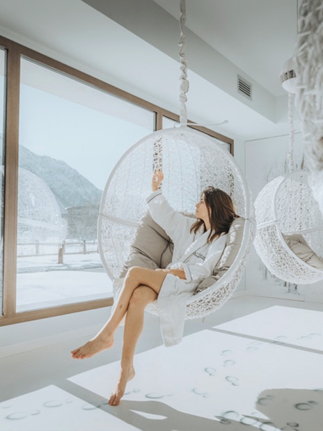 Visitor relaxing in a hanging chair at QC Terme Chamonix Resort & Spa with snowy mountain view.
