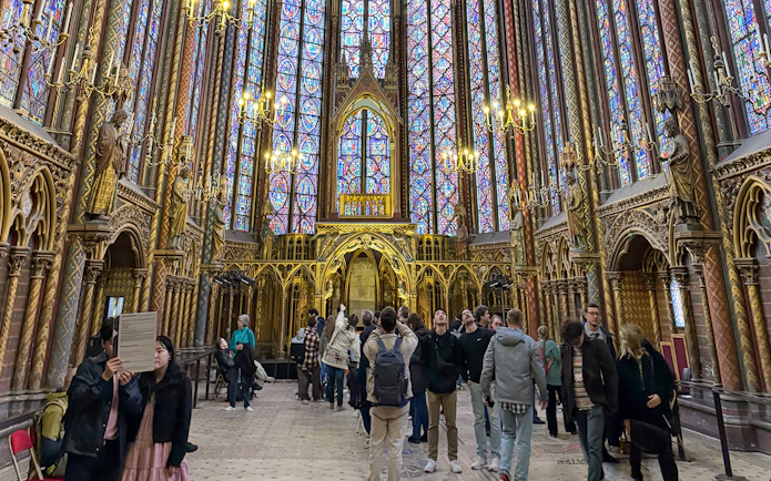 Visitors inside Sainte Chapelle, Paris, admiring stained glass windows and Gothic architecture.