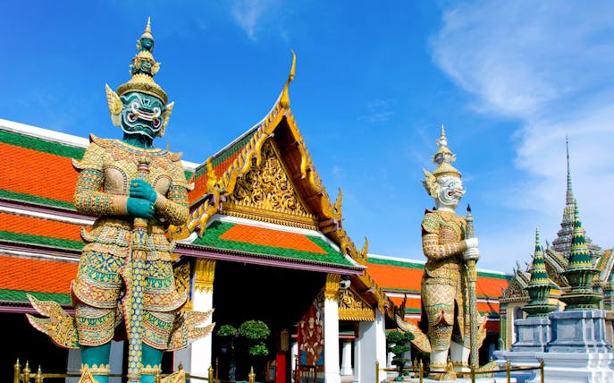 Giant guardian statues at The Grand Palace, Bangkok, on a sunny day.