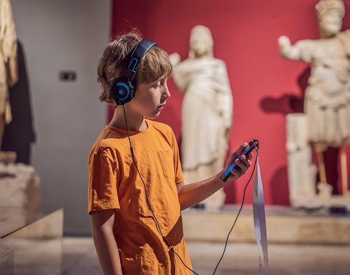 Child with audio guide exploring statues at Accademia Gallery, Florence.