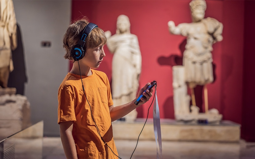 Child with audio guide exploring statues at Accademia Gallery, Florence.