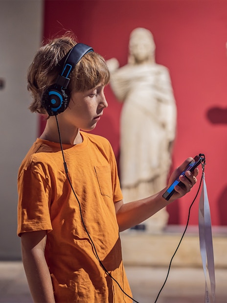 Child with audio guide exploring statues at Accademia Gallery, Florence.