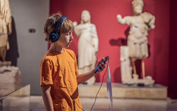 Child with audio guide exploring statues at Accademia Gallery, Florence.