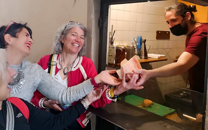 Tourists receiving food from a vendor during a guided street food tour in Florence.