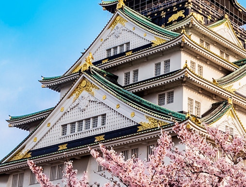 Osaka Castle with cherry blossoms in full bloom under a clear blue sky.