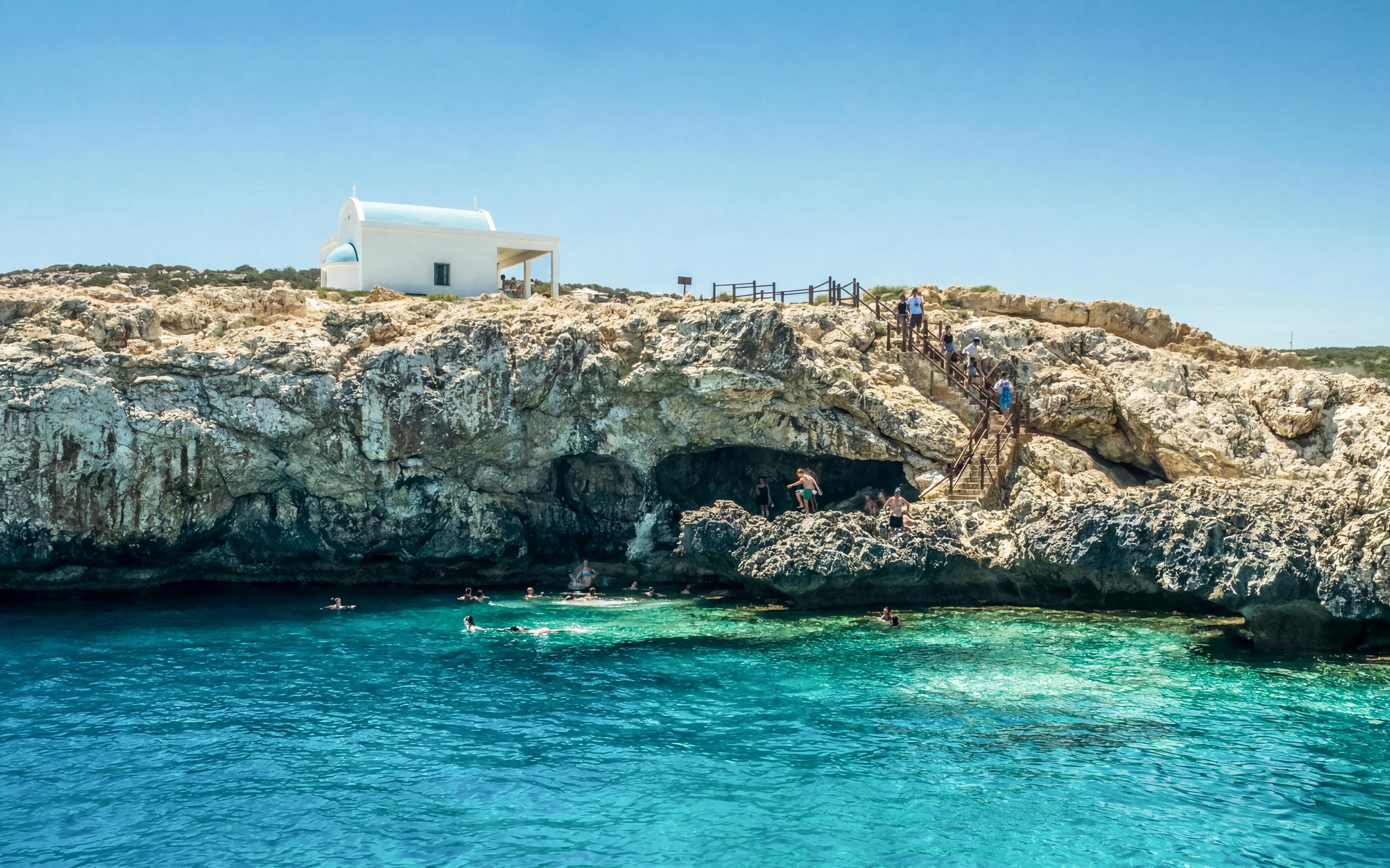 Swimmers explore Blue Lagoon caves near Protaras with a white chapel on the cliff.