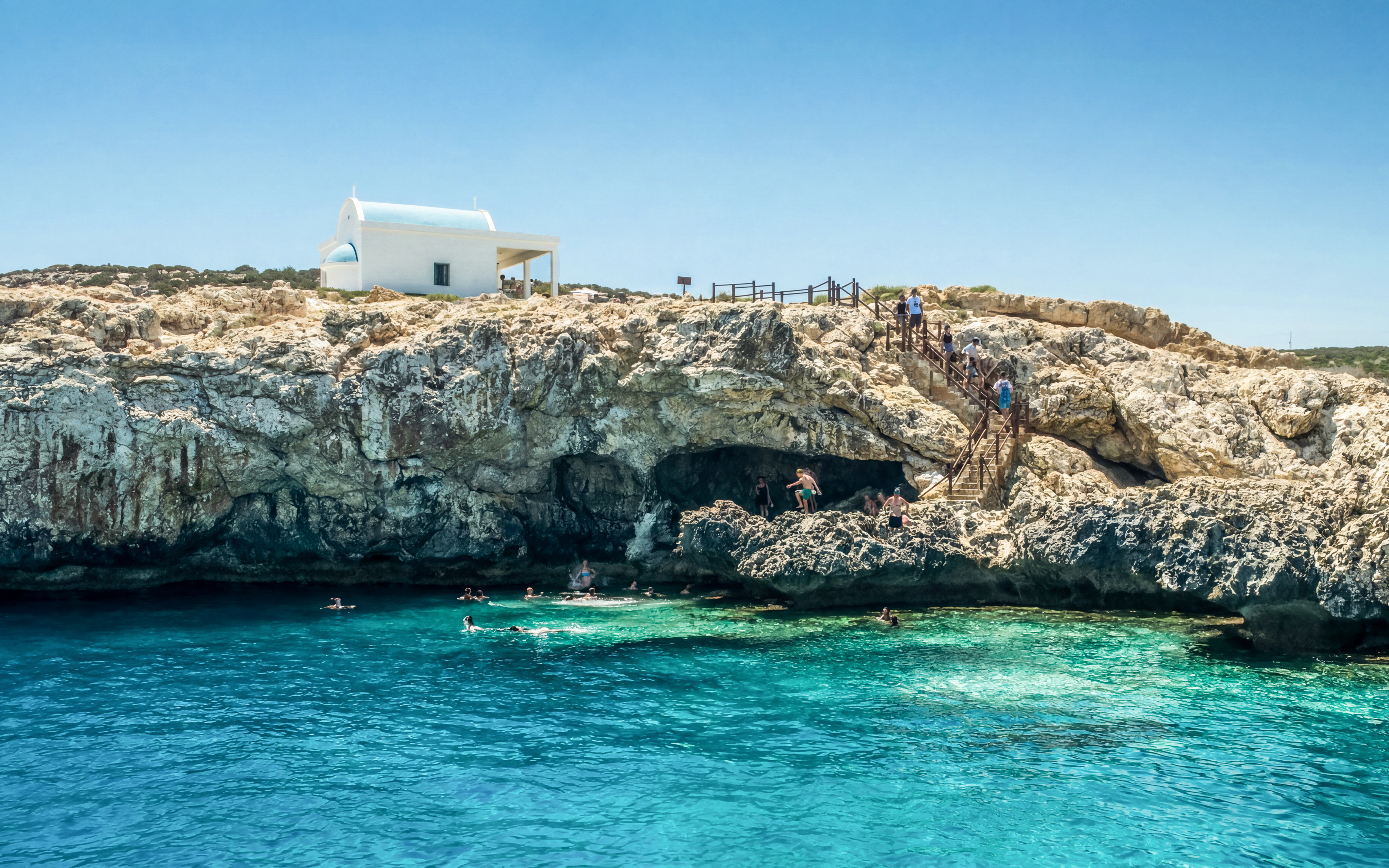 Swimmers explore Blue Lagoon caves near Protaras with a white chapel on the cliff.
