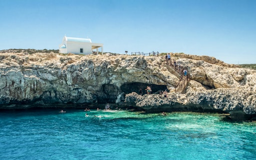Swimmers explore Blue Lagoon caves near Protaras with a white chapel on the cliff.