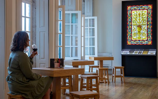 Visitor enjoying wine at Museu do Vitral in Porto, with stained glass display.