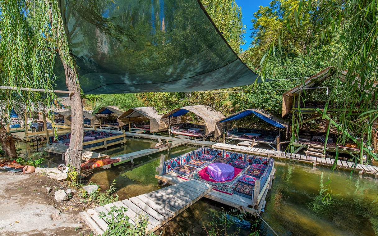 Outdoor seating area with traditional rugs over a stream in Cappadocia, Turkey.