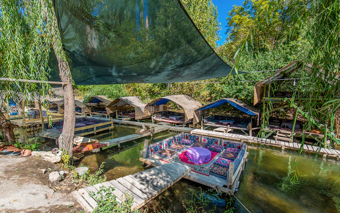 Outdoor seating area with traditional rugs over a stream in Cappadocia, Turkey.