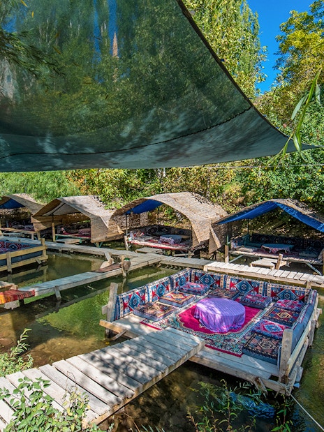 Outdoor seating area with traditional rugs over a stream in Cappadocia, Turkey.