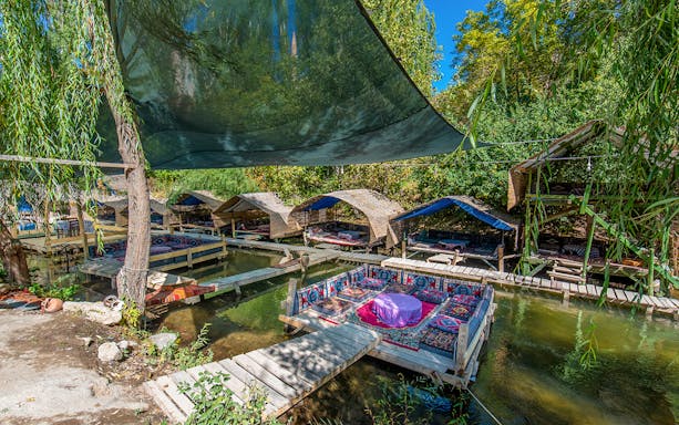 Outdoor seating area with traditional rugs over a stream in Cappadocia, Turkey.