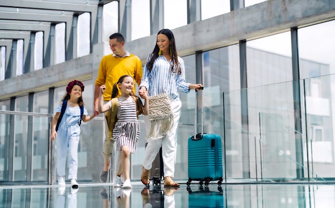 Family walking with luggage at Hong Kong Airport terminal.