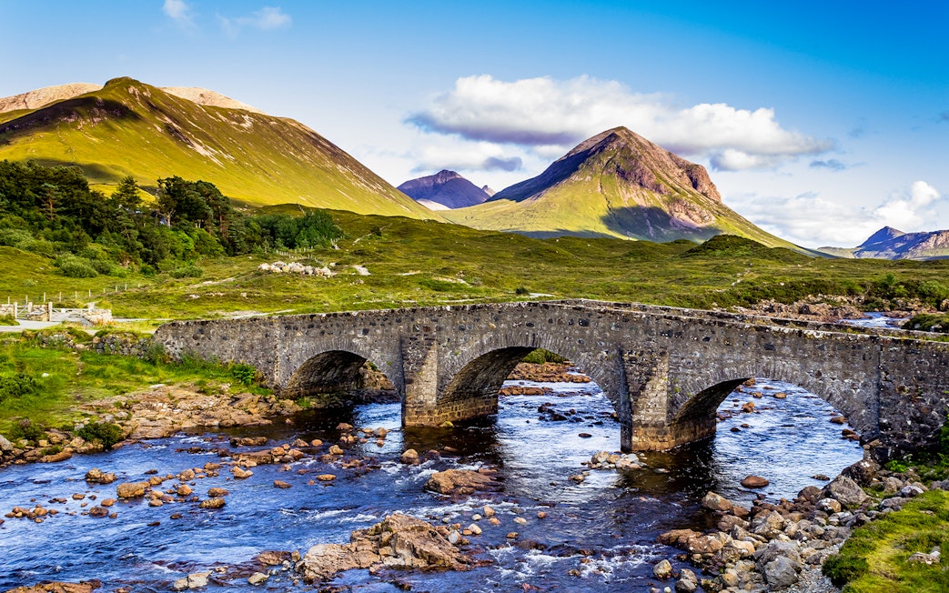 Stone bridge over river with Scottish Highlands in the background.