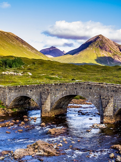 Stone bridge over river with Scottish Highlands in the background.