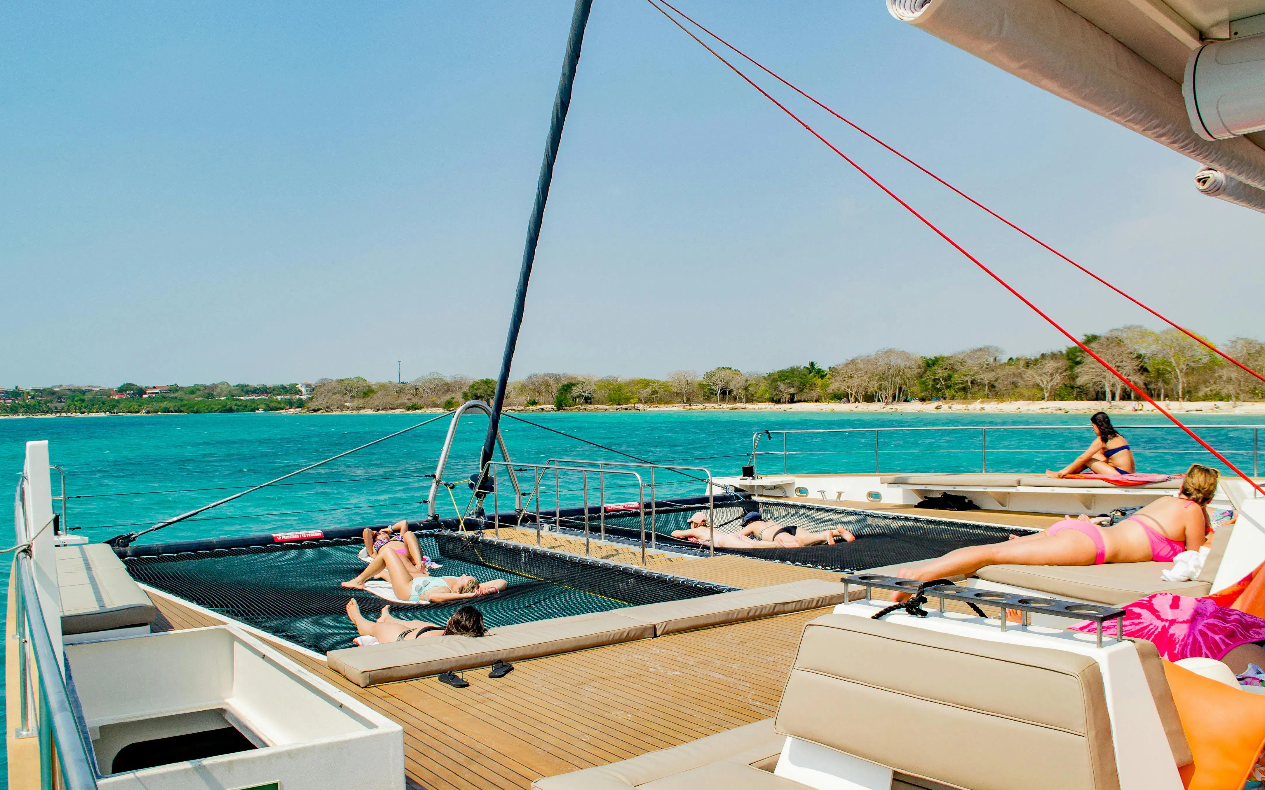 Catamaran deck with people sunbathing, turquoise sea, Rosario Islands in background.
