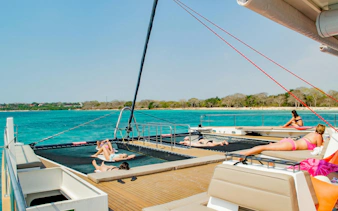 Catamaran deck with people sunbathing, turquoise sea, Rosario Islands in background.