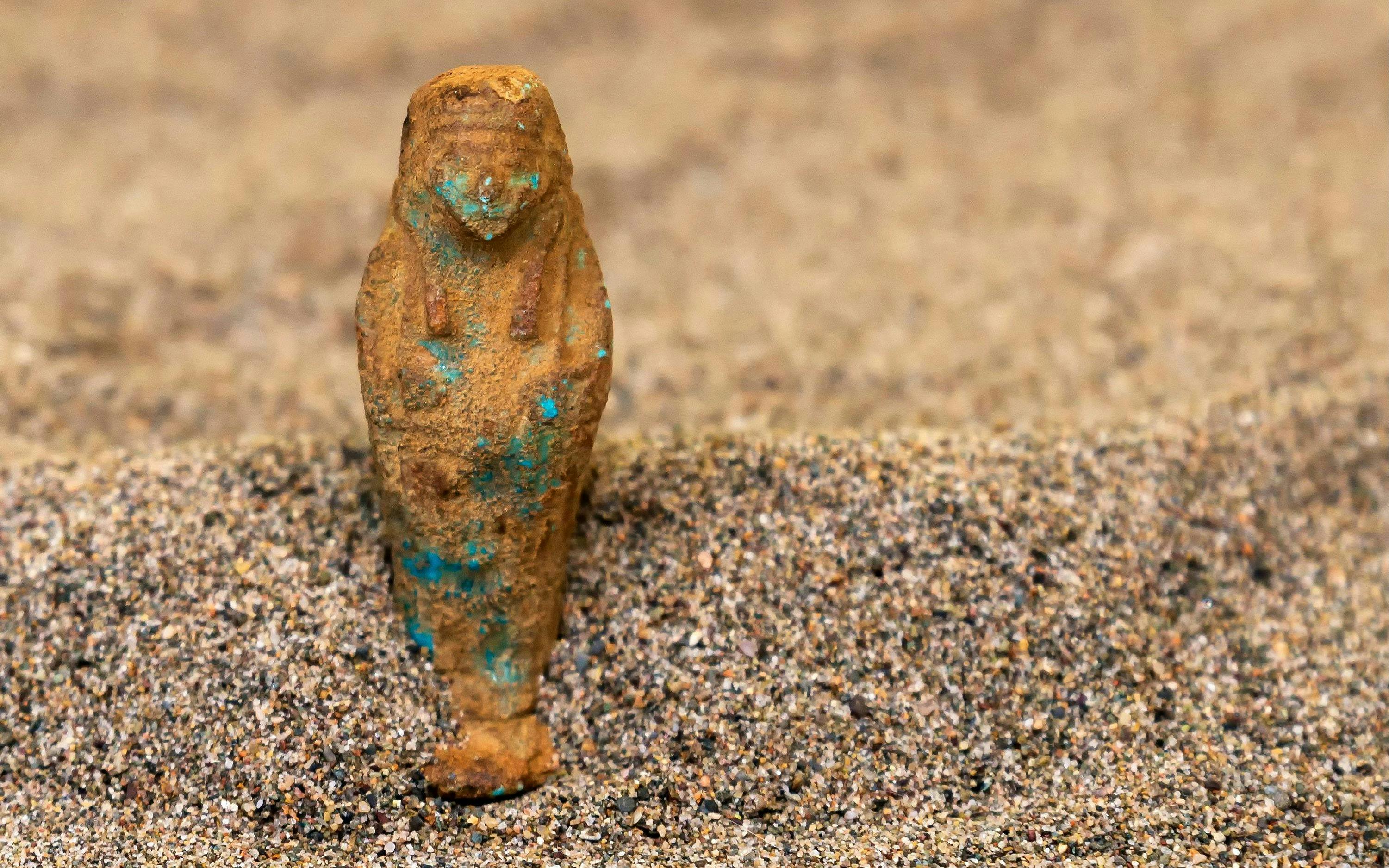 Shabti figurine partially buried in sand.