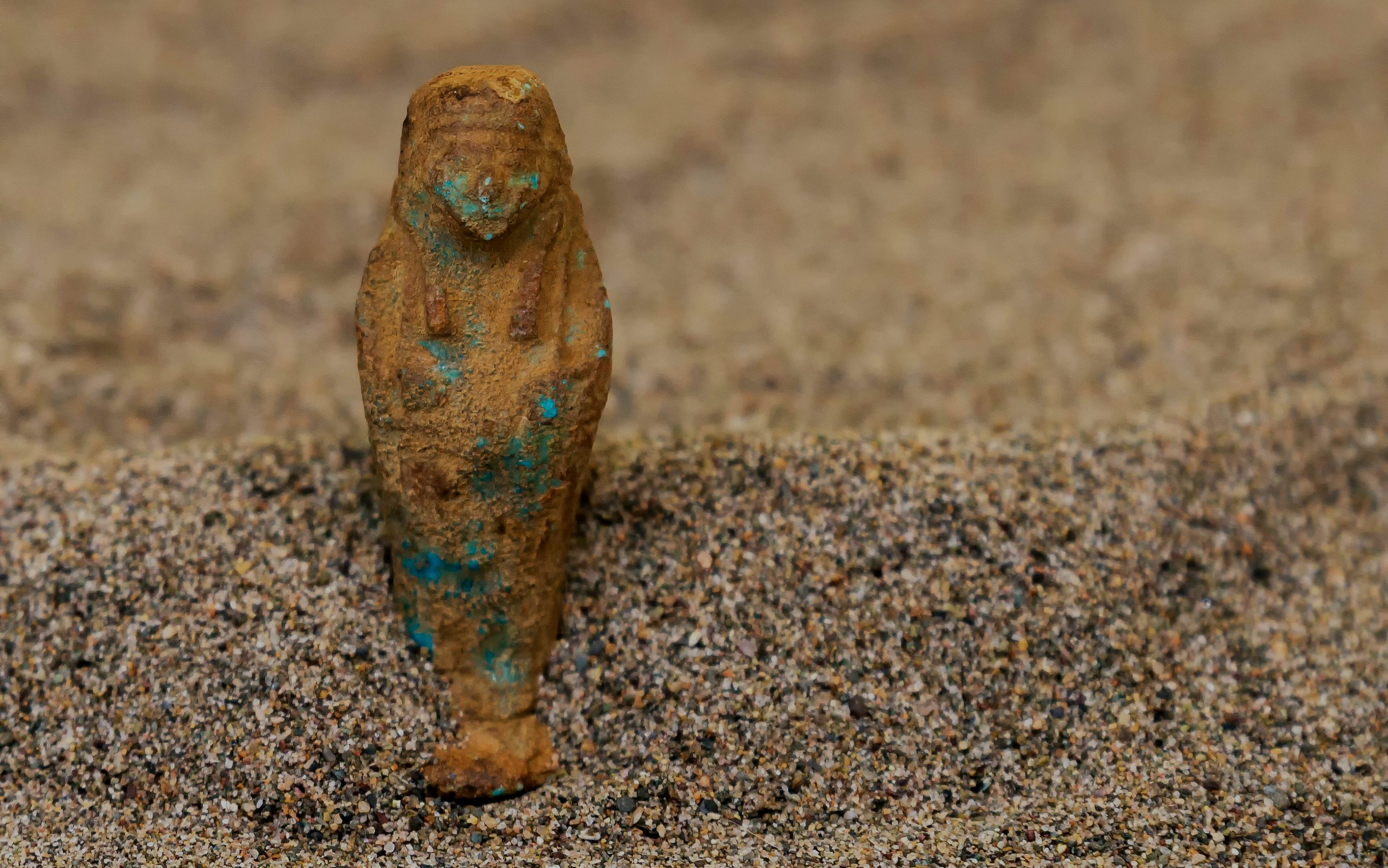 Shabti figurine partially buried in sand.