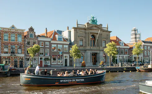 Boat tour on Haarlem canal passing historic buildings.