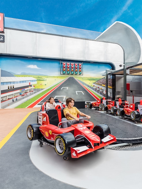 Junior championship ride at Ferrari Land with children in red race cars.