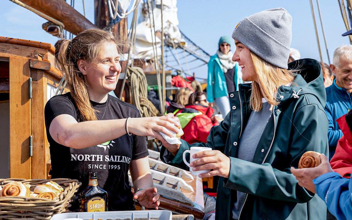 Crew serving hot chocolate and cinnamon buns to guests on a whale watching tour in Husavik.