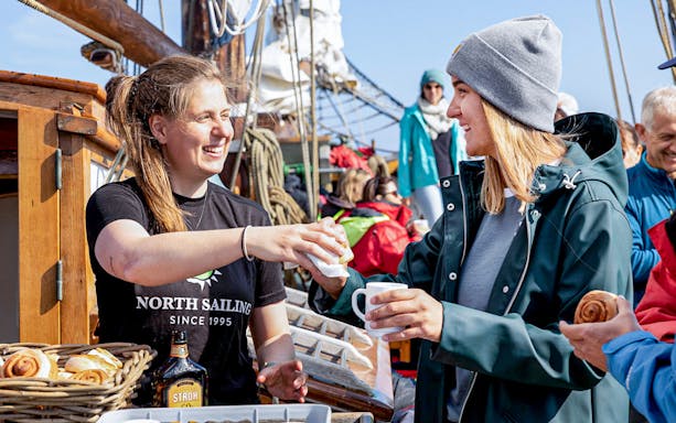 Crew serving hot chocolate and cinnamon buns to guests on a Whale Watching tour in Husavik, Iceland.