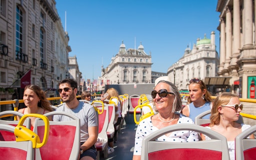Tourists on a Hop-on Hop-off bus tour in London with historic buildings in the background.
